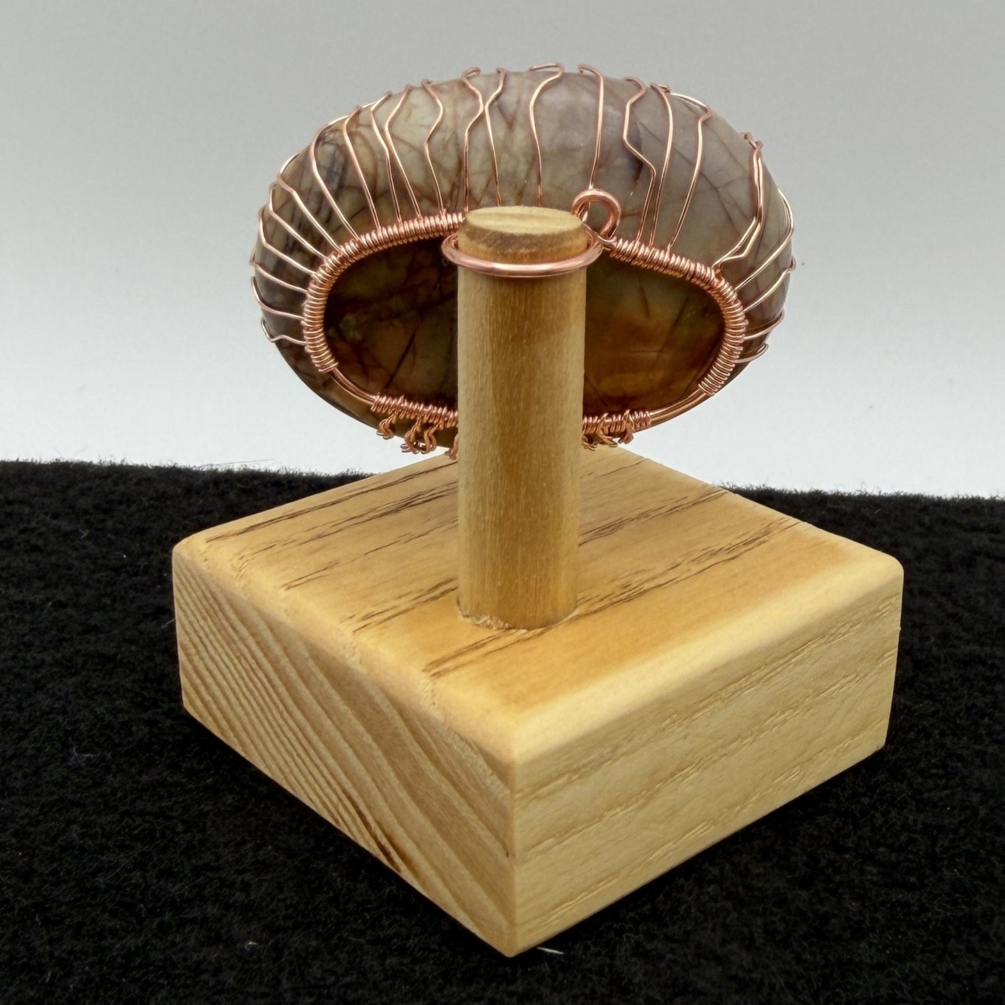 Back view of a decorative tree-of-life sculpture made from polished picasso jasper and copper wire, mounted on a light-colored wooden block against a neutral gray background.
