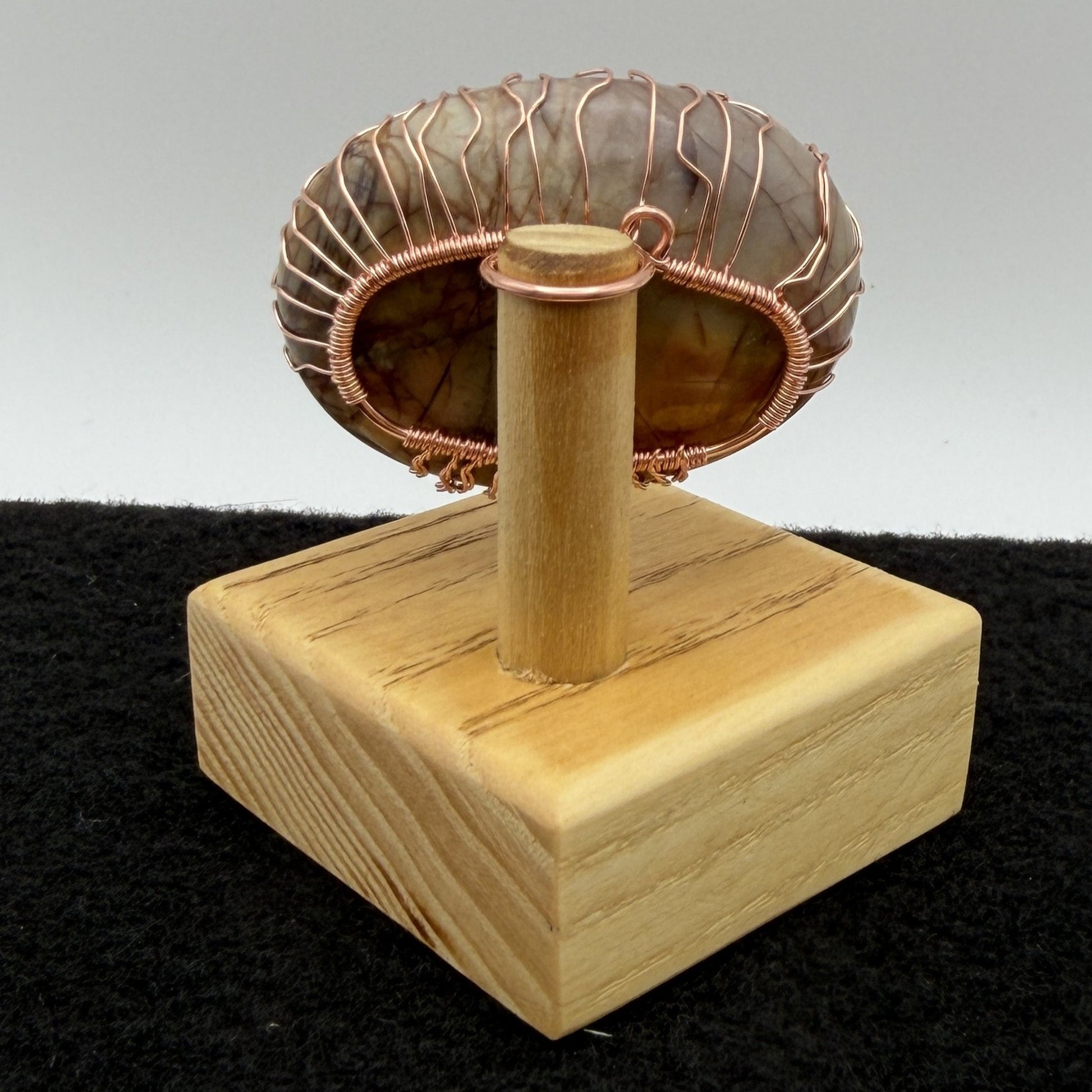Back view of a decorative tree-of-life sculpture made from polished picasso jasper and copper wire, mounted on a light-colored wooden block against a neutral gray background.