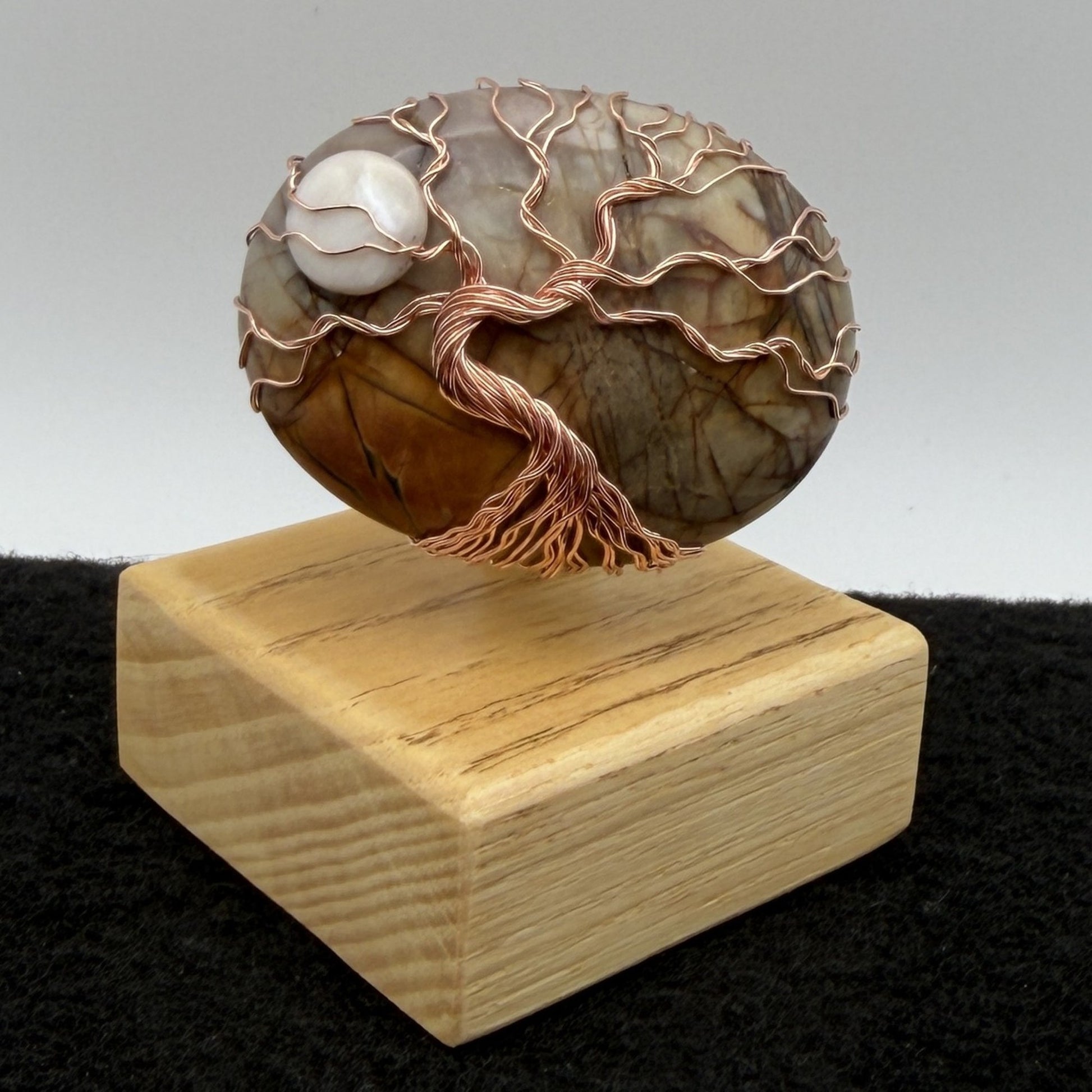 Front view of a decorative tree-of-life sculpture made from polished picasso jasper and copper wire, mounted on a light-colored wooden block against a neutral gray background.