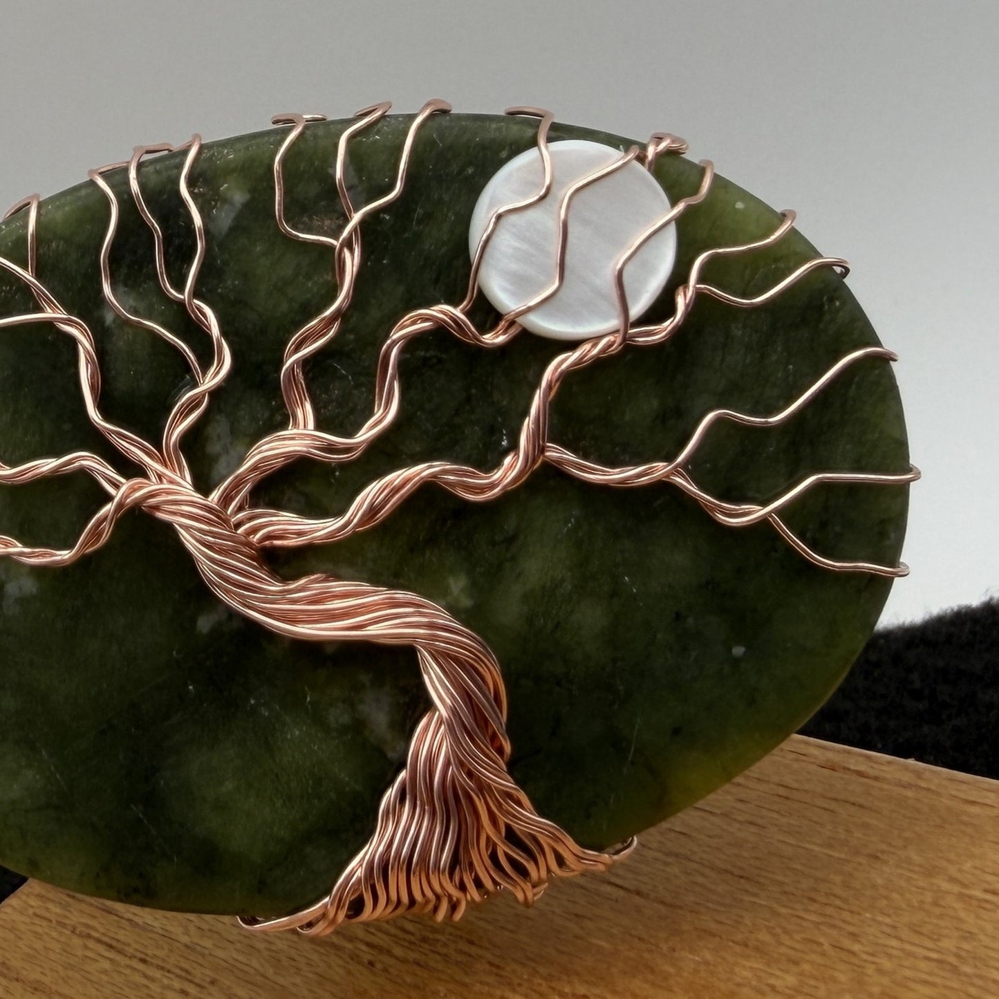 Detail view of a tree of life display piece featuring a green serpentine stone with copper wire roots and branches and a white moon, mounted on a square wooden display block.