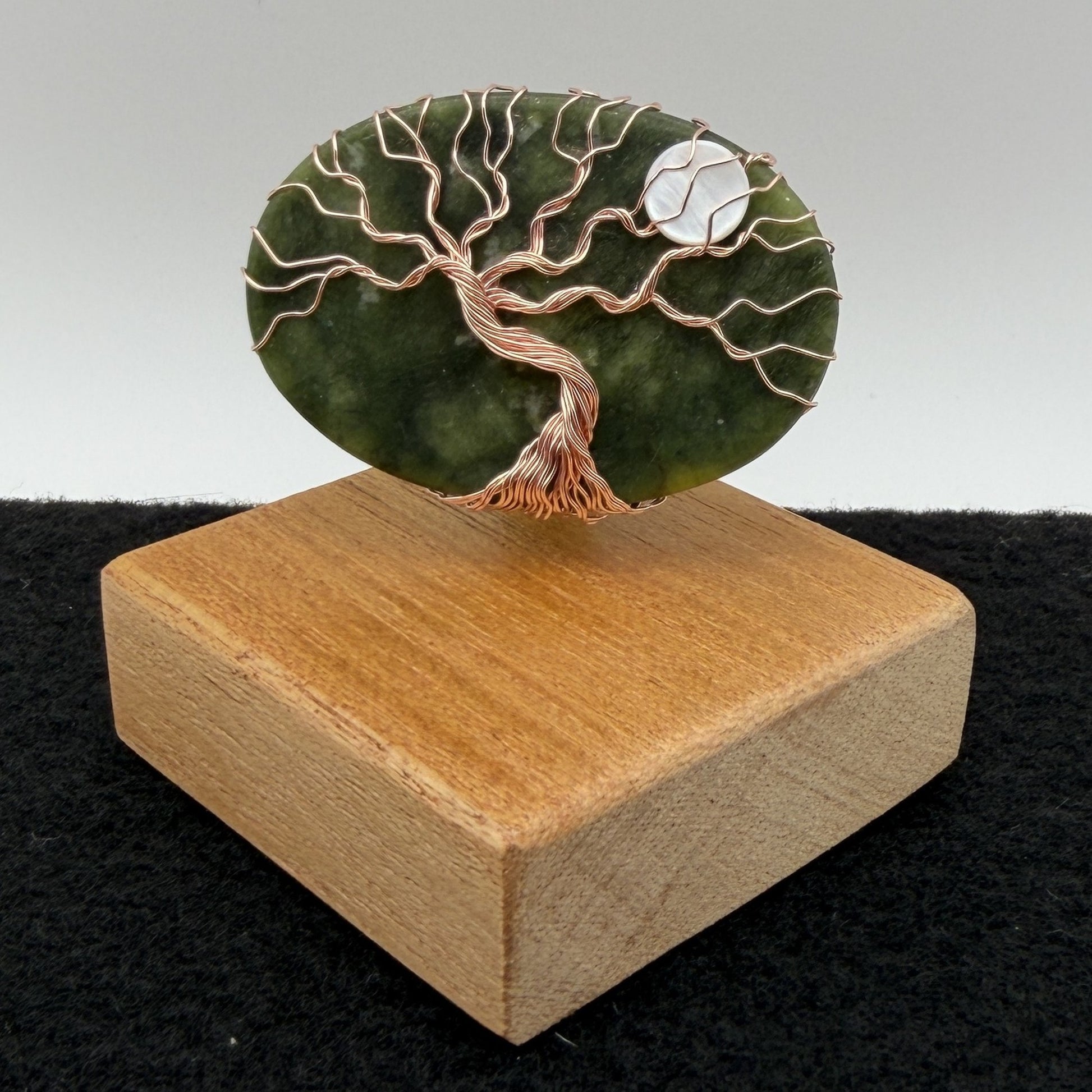 Front view of a tree of life display piece featuring a green serpentine stone with copper wire roots and branches and a white moon, mounted on a square wooden display block.
