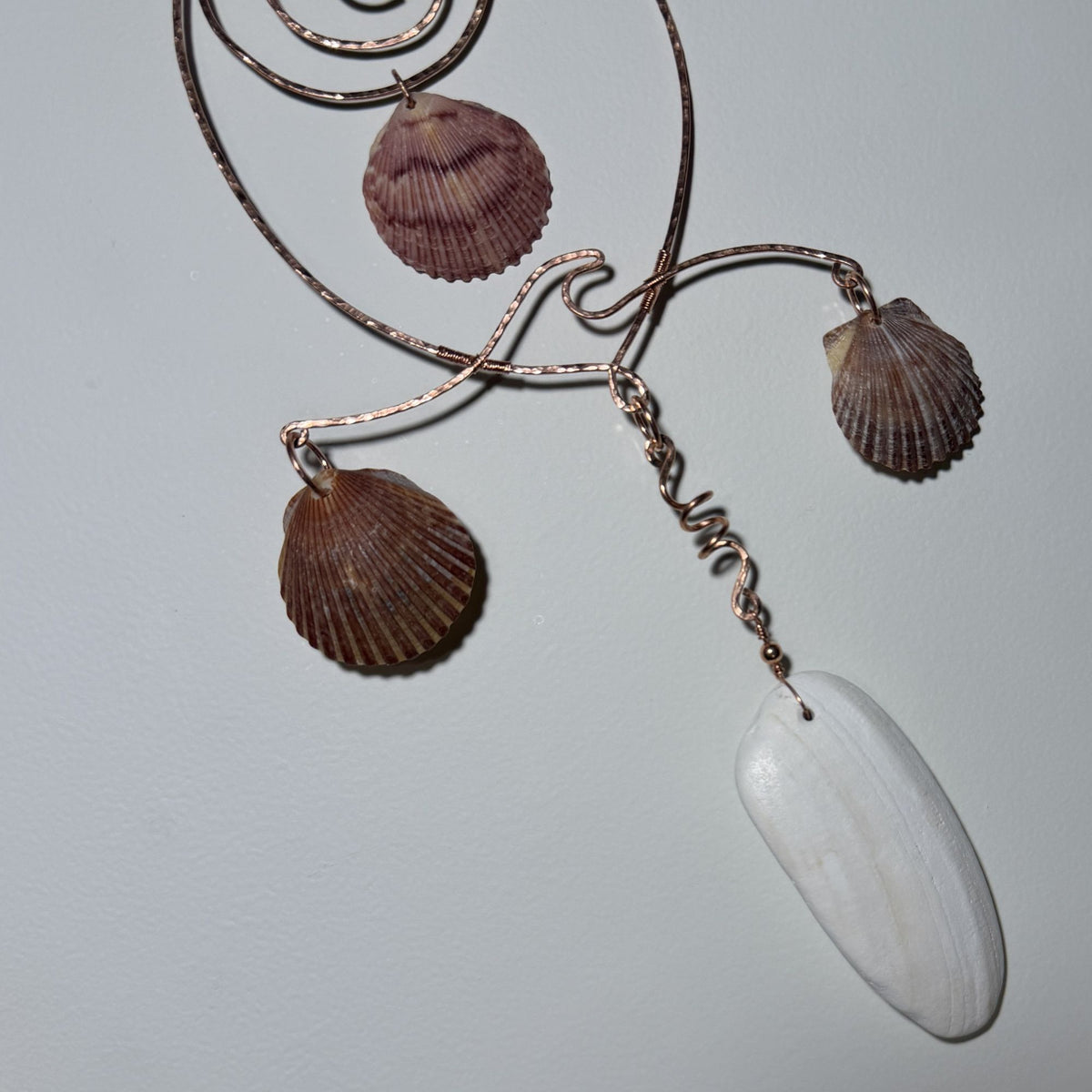Detail view of a shell and hammered copper wire wall/window display piece.