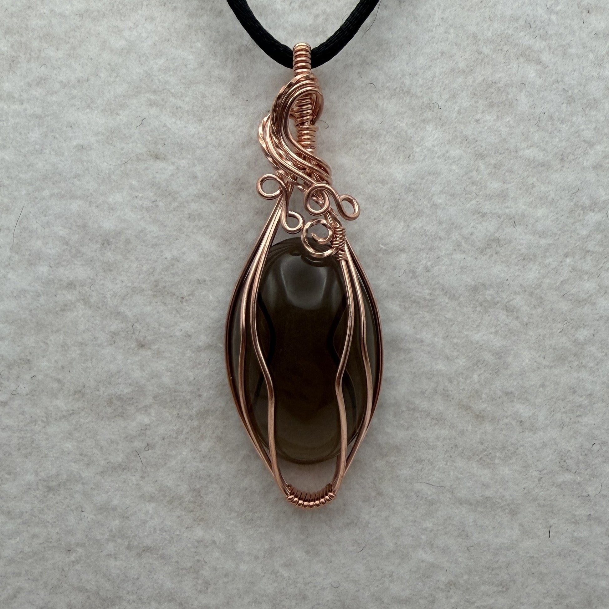Front view of a teardrop-shaped dark brown smoky quartz stone pendant wrapped in copper wire, hanging from a black cord on a textured white background.