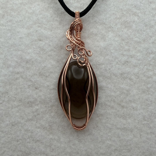 Front view of a teardrop-shaped dark brown smoky quartz stone pendant wrapped in copper wire, hanging from a black cord on a textured white background.