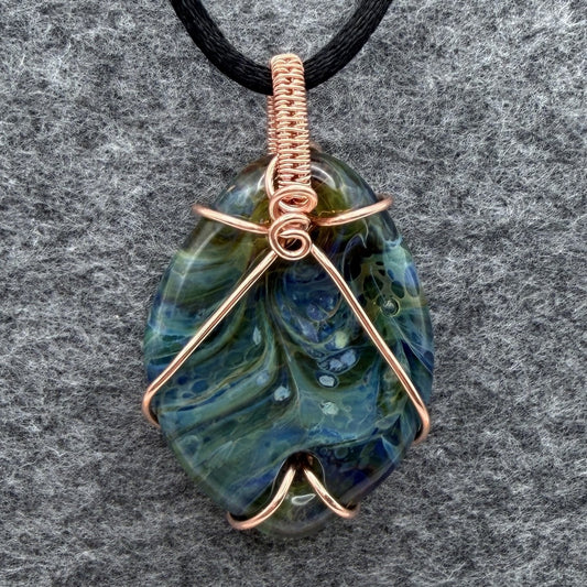 Front view of side 1 of a handmade pendant necklace featuring a marbled blue and green glass stone wrapped in copper wire, hanging from a black cord against a textured gray background.