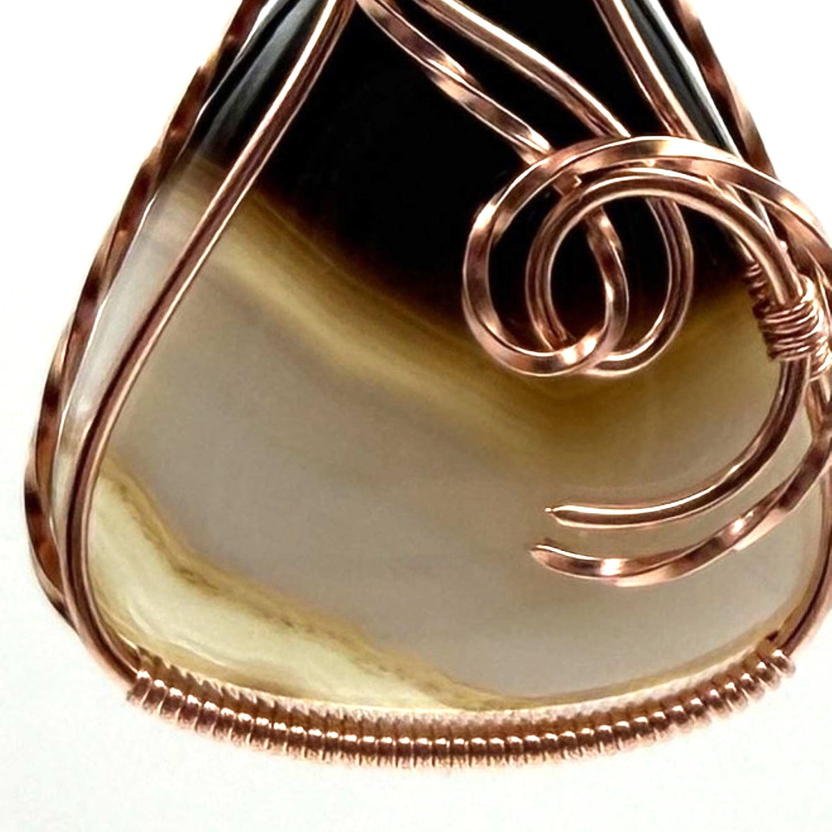 Detail view of a teardrop shaped Botswana agate wrapped in copper wire, held by a black cord on a gray felt backdrop.